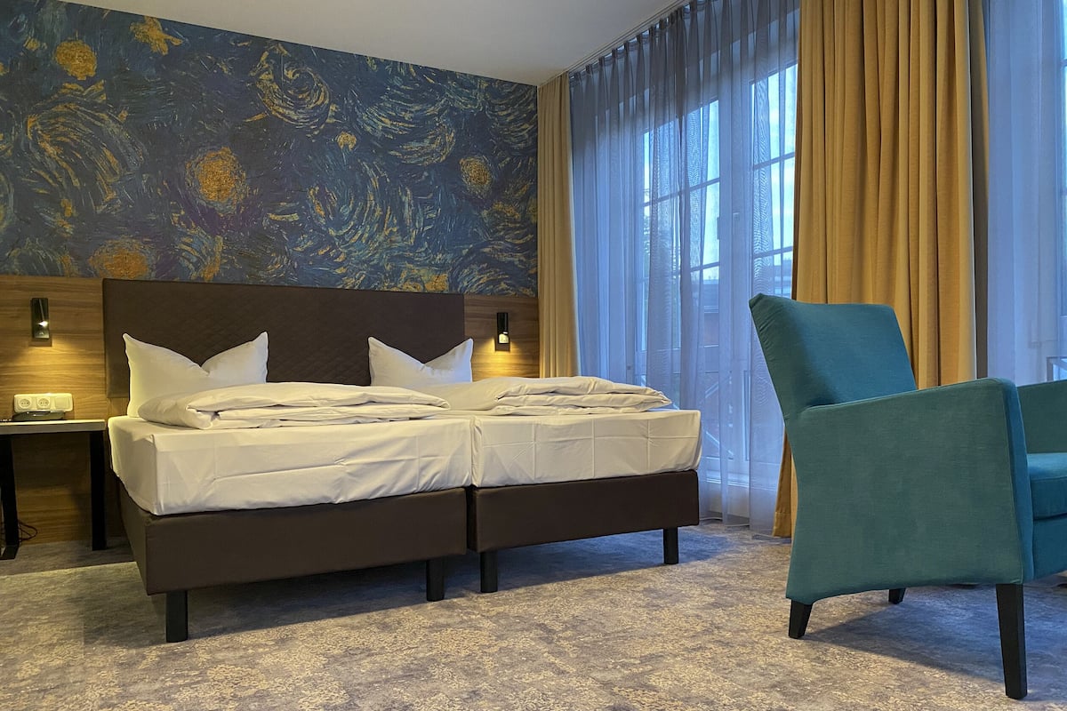 A hotel room with a large bed, a chair, a nightstand, and a wall with a painting.