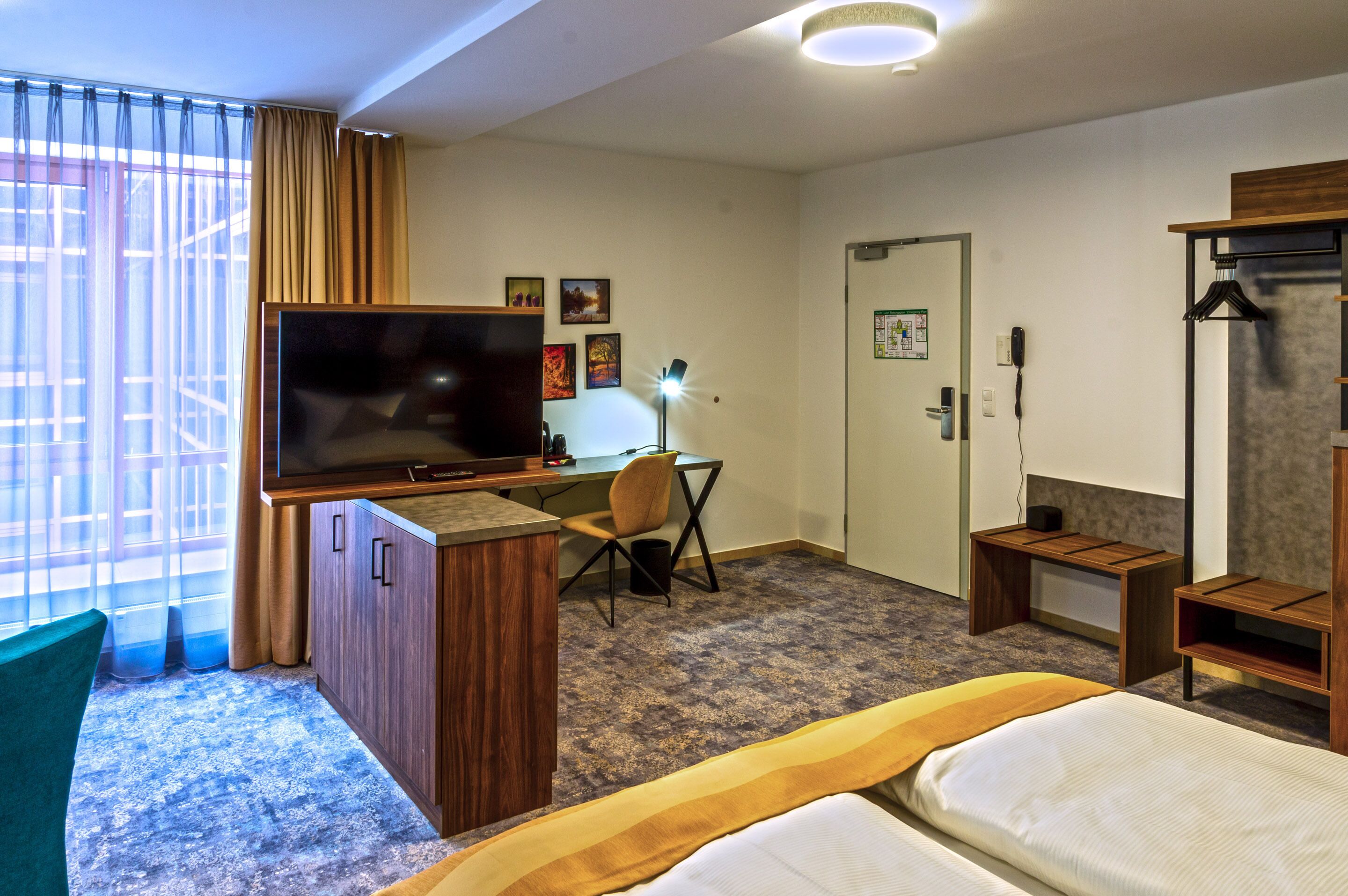 A hotel room with a bed, a desk with a television, a chair, and a wardrobe.