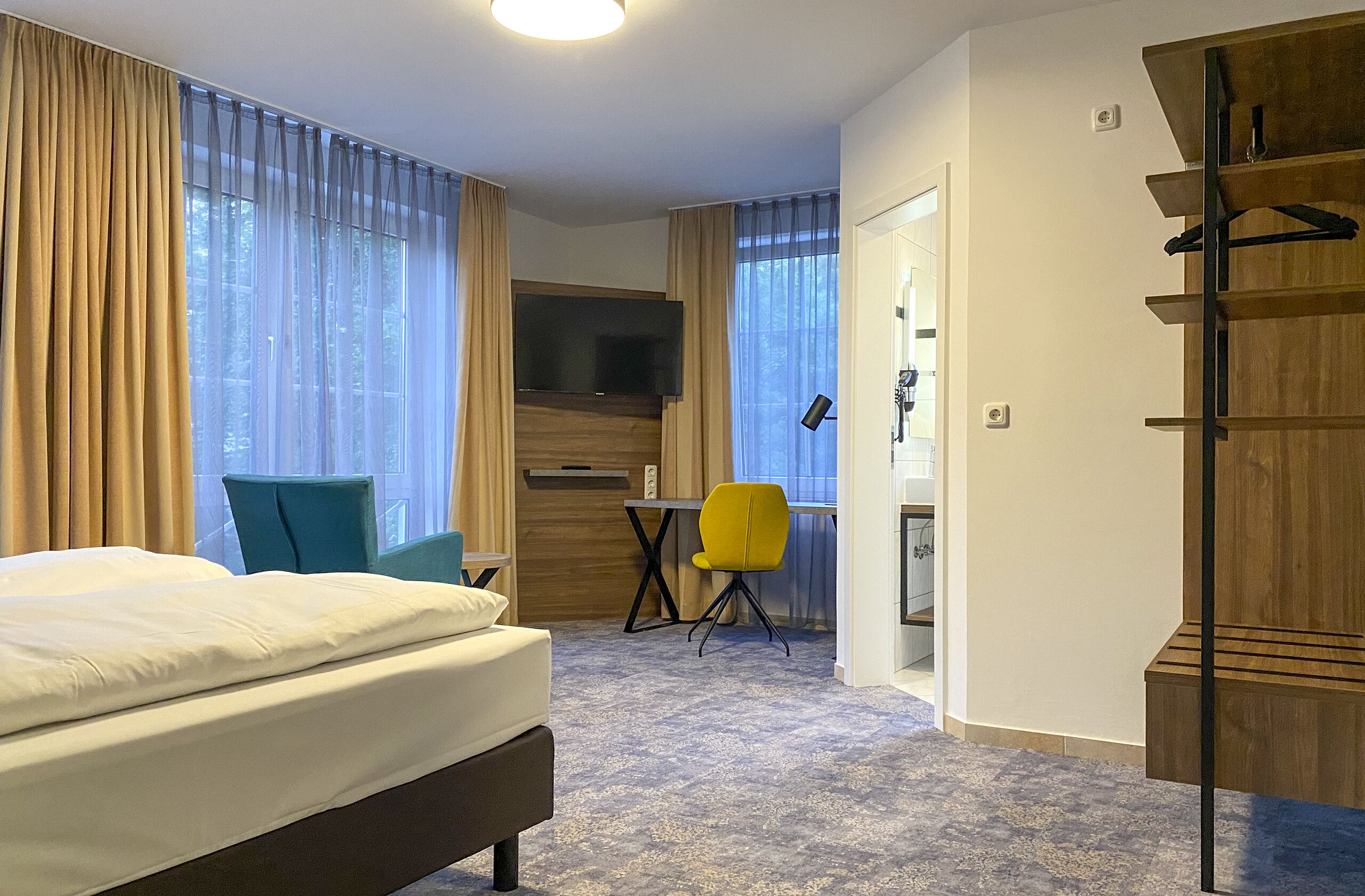 Una habitación de hotel con cama, escritorio, silla, televisor y armario.
