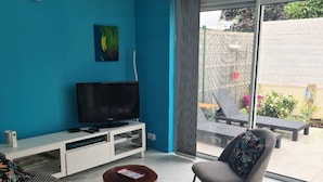 Un saló amb televisió, sofà i cadira, una finestra amb vista a l'exterior i una paret blava.