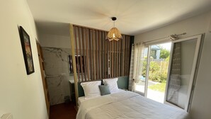 A bedroom with a large bed, a wooden headboard, a hanging light fixture, and a view of the outdoors through a glass door. - 600m Plage (Saint-Palais-sur-Mer)