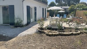 A patio area with a table and chairs, a bicycle, and a white building with blue shutters. - 600m Plage (Saint-Palais-sur-Mer)