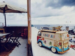 Um ônibus decorado com flores estacionado em um terraço, com vista para o mar e edifícios ao fundo.