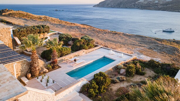 A pool with a view of the sea, surrounded by greenery and a stone pathway. - Villa Hola Mykonos (Mykonos)