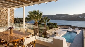 A covered outdoor area with a pool, seating, and a view of the sea. - Villa Hola Mykonos (Mykonos)