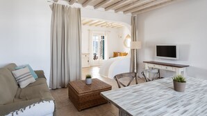 A living room with a sofa, a table, a TV, and a wicker ottoman. - Villa Hola Mykonos (Mykonos)