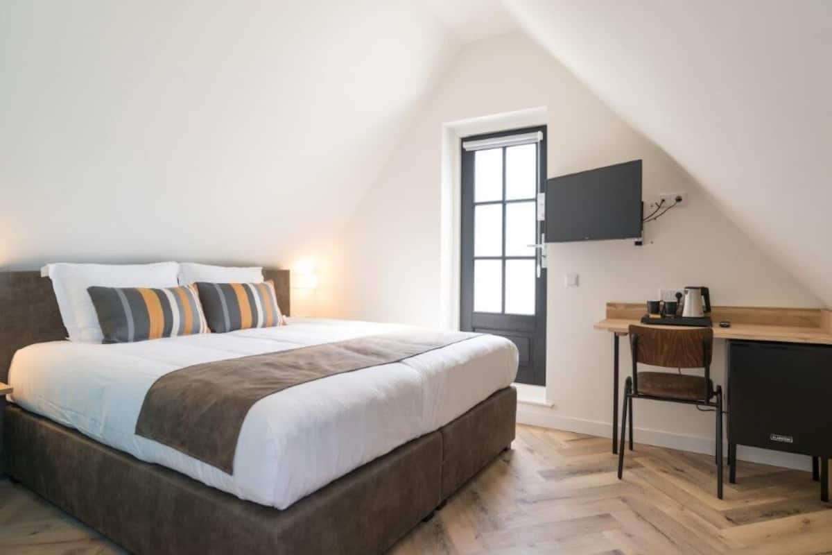 A bedroom with a bed, a desk, a chair, and a TV mounted on the wall.