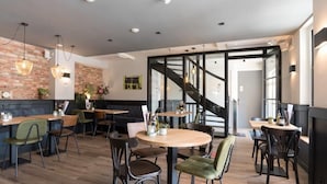 Un restaurante moderno con mesas y sillas de madera, pared de ladrillo y una escalera que sube a un nivel superior.