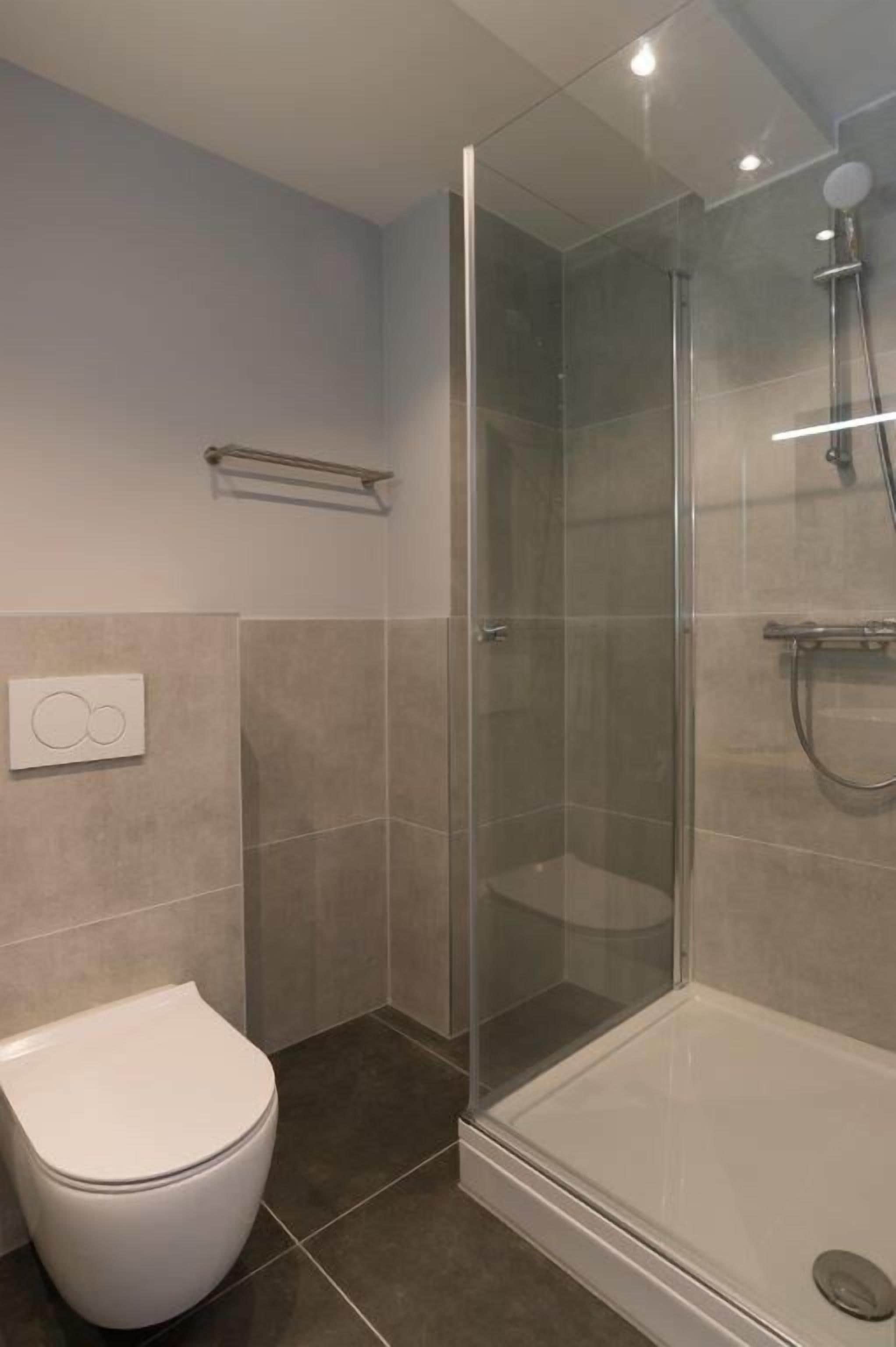 A modern bathroom with a glass-enclosed shower, a white toilet, and a towel rack.