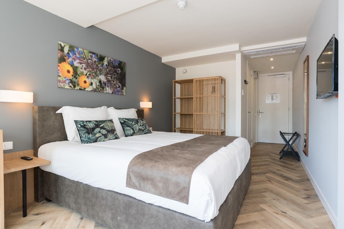 A modern bedroom with a large bed, a nightstand, a wooden wardrobe, and a painting on the wall.