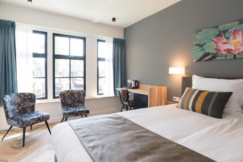 Una habitación de hotel con una cama grande, dos sillones florales, un escritorio con silla y un cuadro de una flor de loto en la pared.