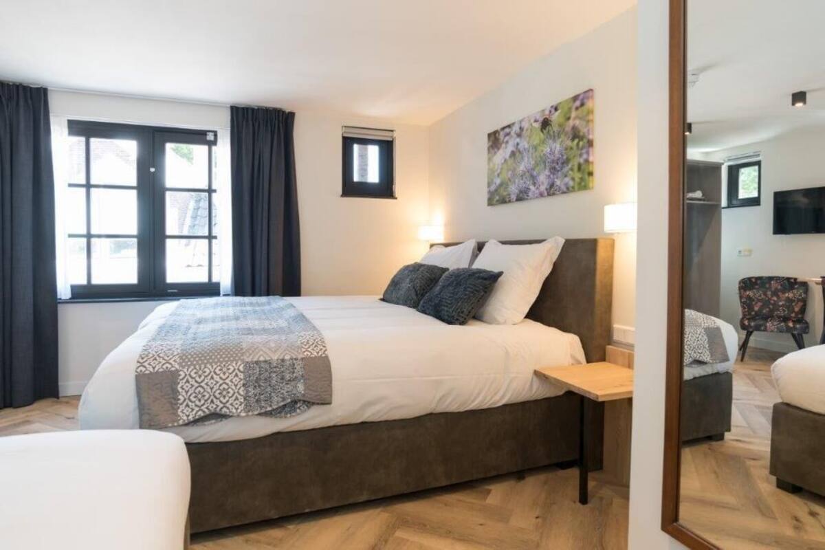 A modern bedroom with a large bed, bedside tables, a small window, and a painting on the wall.