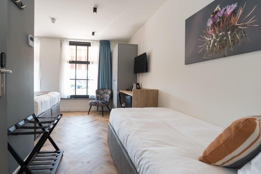 Une chambre d’hôtel avec deux lits, un bureau, une chaise, une télévision et une fenêtre avec des rideaux.