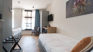 Une chambre d’hôtel avec deux lits, un bureau, une chaise, une télévision et une fenêtre avec des rideaux.