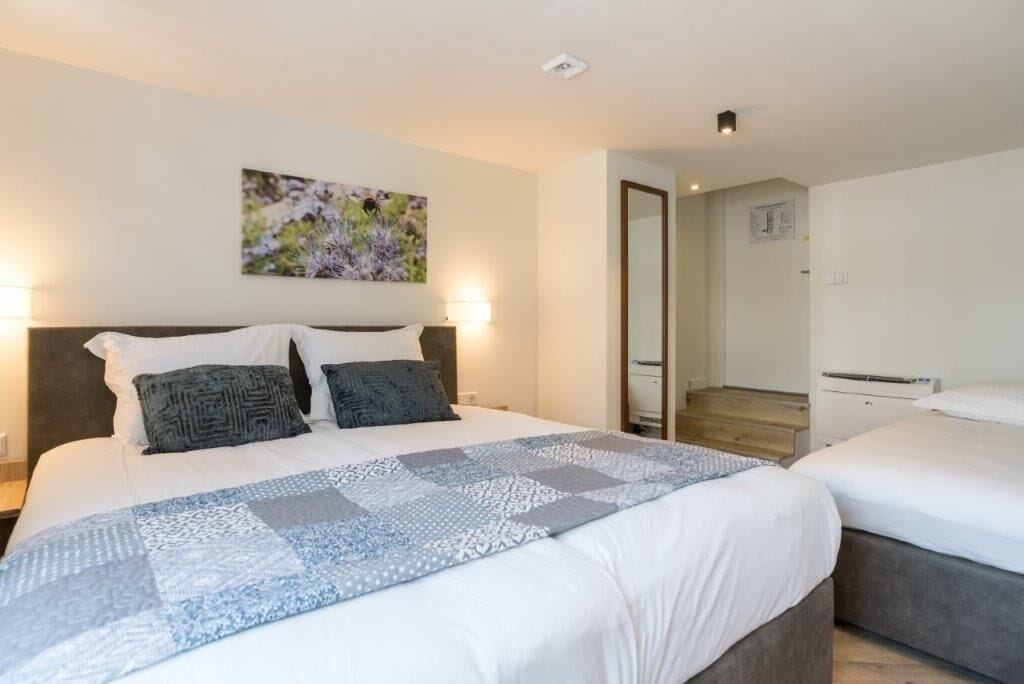 Una habitación de hotel con una cama grande, dos mesitas de noche, una lámpara de pared y un cuadro.