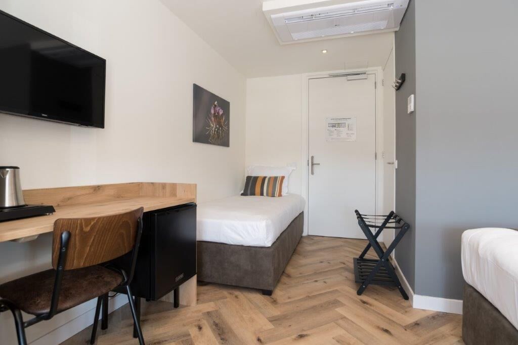 Une pièce de taille modeste comprenant un lit, un bureau, une chaise, un téléviseur et une petite kitchenette.