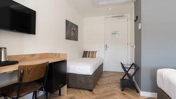 Una habitación pequeña con cama, escritorio, silla, televisor y una kitchenette.