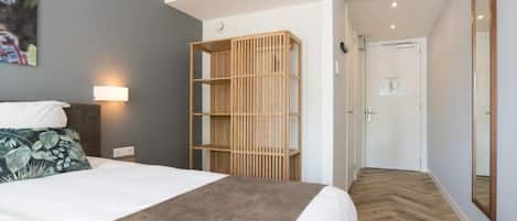 Een hotelkamer met een bed, een houten boekenkast, een wandlamp en een spiegel.
