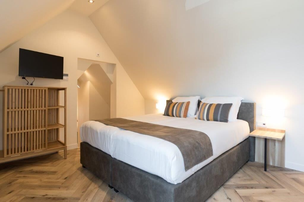 Ein Schlafzimmer mit einem großen Bett, einem an der Wand befestigten Fernseher und einem Holzregal.