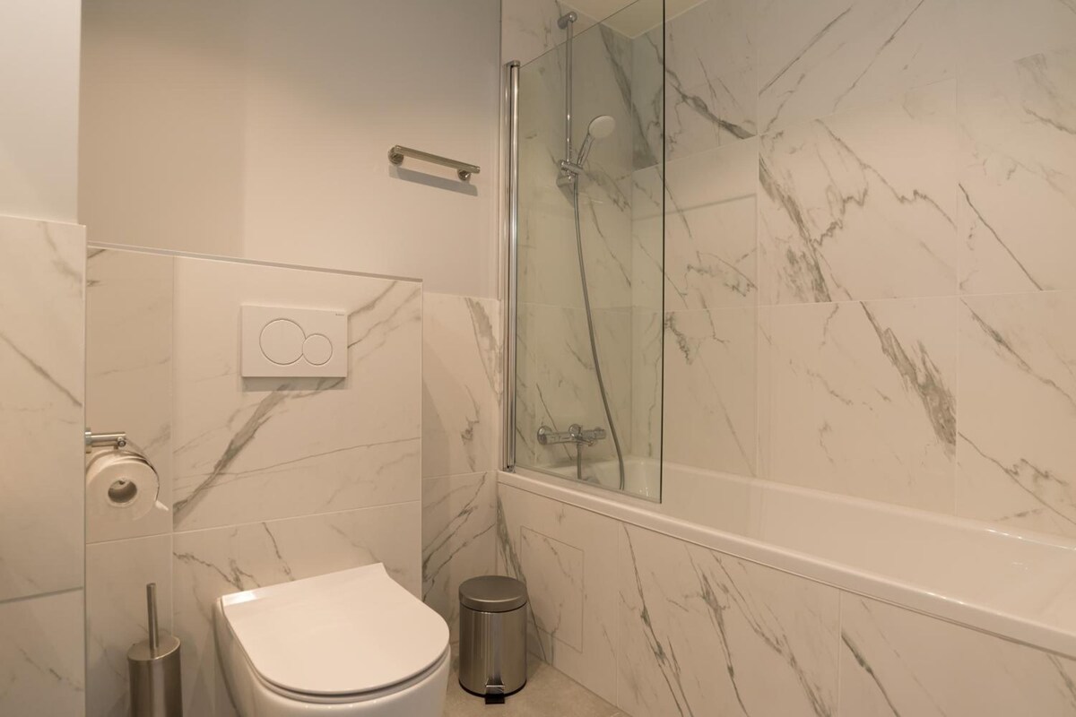 A bathroom with a toilet, a bidet, a trash bin, and a glass-enclosed shower area.