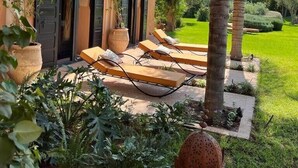 Une maison avec un jardin, des palmiers et un espace salon extérieur.