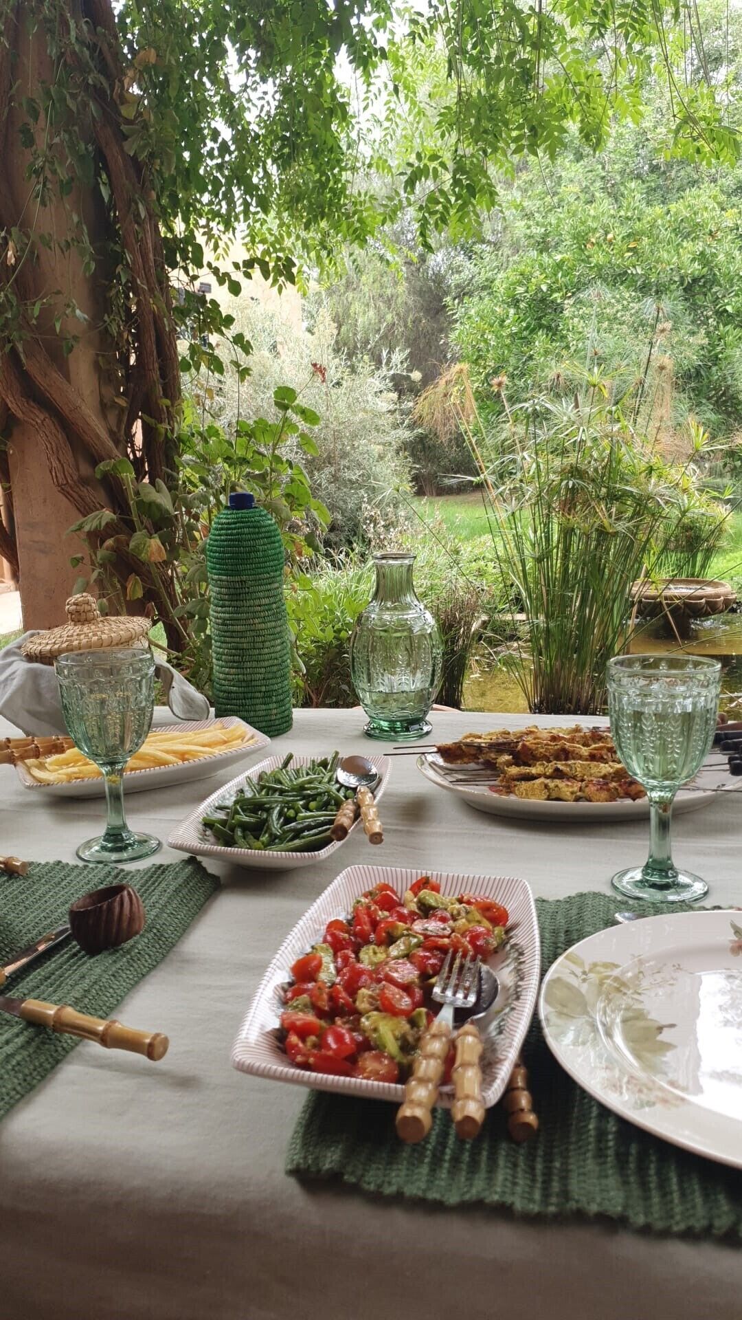 Mesa de comedor al aire libre con varios platos, vasos y una decoración rústica en un jardín.