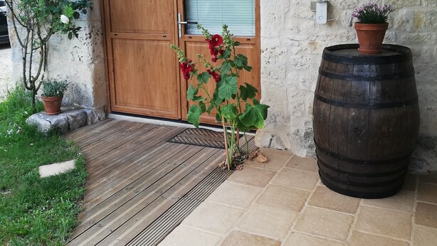 Eine Holztür mit Fensterglas, ein Blumentopf, ein Holzbottich und ein kleiner Gartenbereich mit einem gepflasterten Weg.