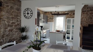 A dining area with a stone wall, a clock, and a view into the kitchen. - House 6 pers beach 3km town center 5mn walk (Crozon)