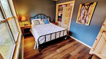 A bedroom with a bed, wooden floor, a ceiling fan, a nightstand, a window, and a wardrobe.