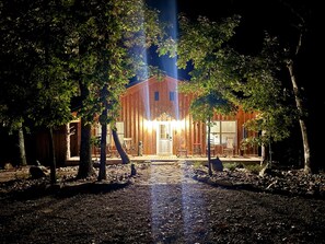 Un bâtiment en bois doté d’un porche à l’avant, entouré d’arbres, et un chemin menant à l’entrée.