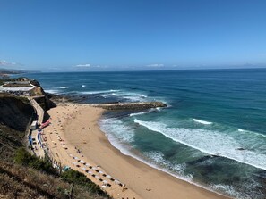 Une plage côtière avec un rivage rocheux, une promenade dallée et des parasols.