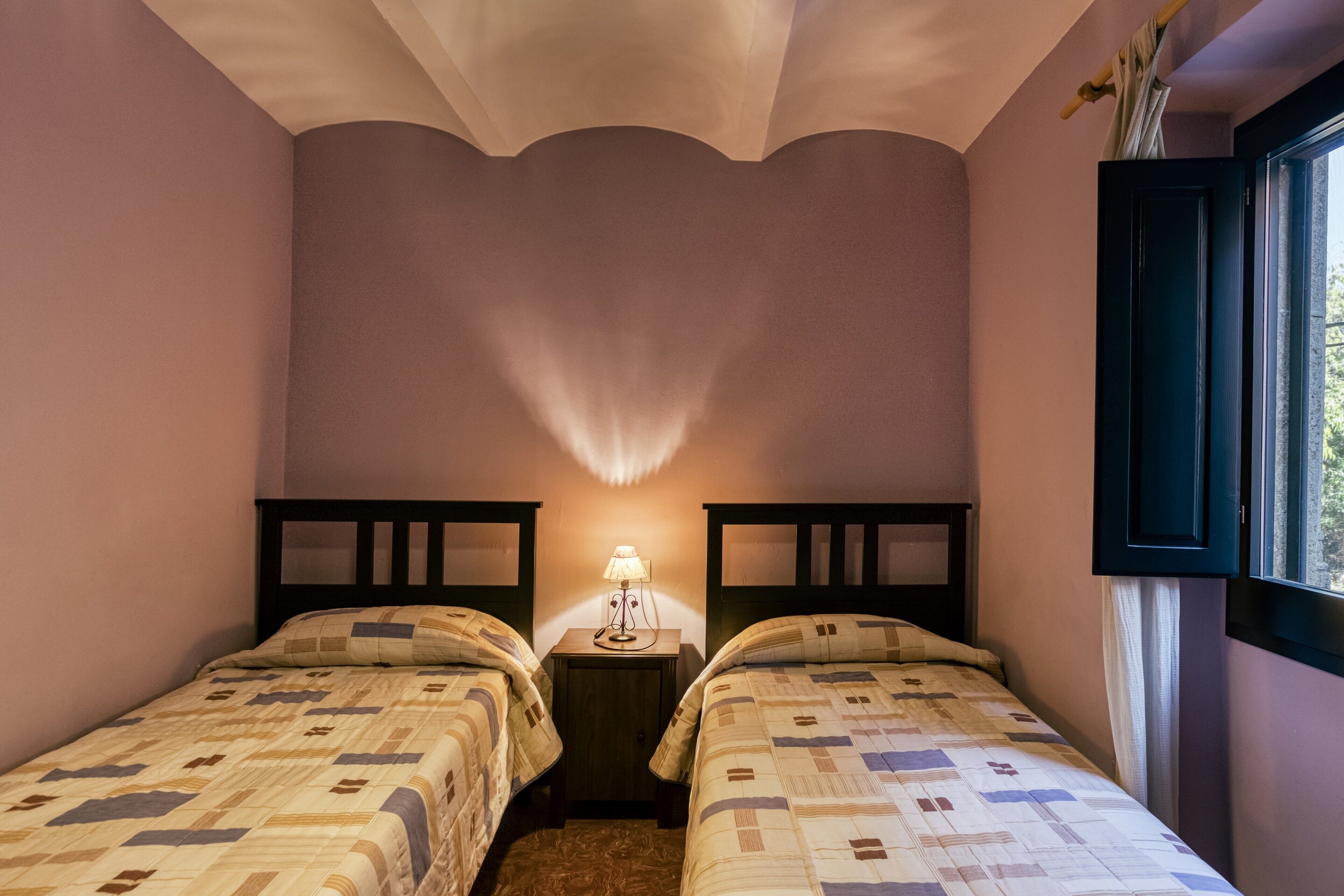 A bedroom with two beds, a nightstand with a lamp, and a window with curtains.