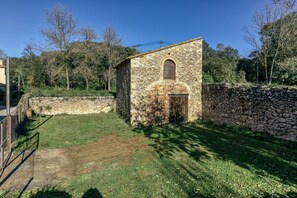A stone building with a small arched window, surrounded by a stone wall and a grassy area.