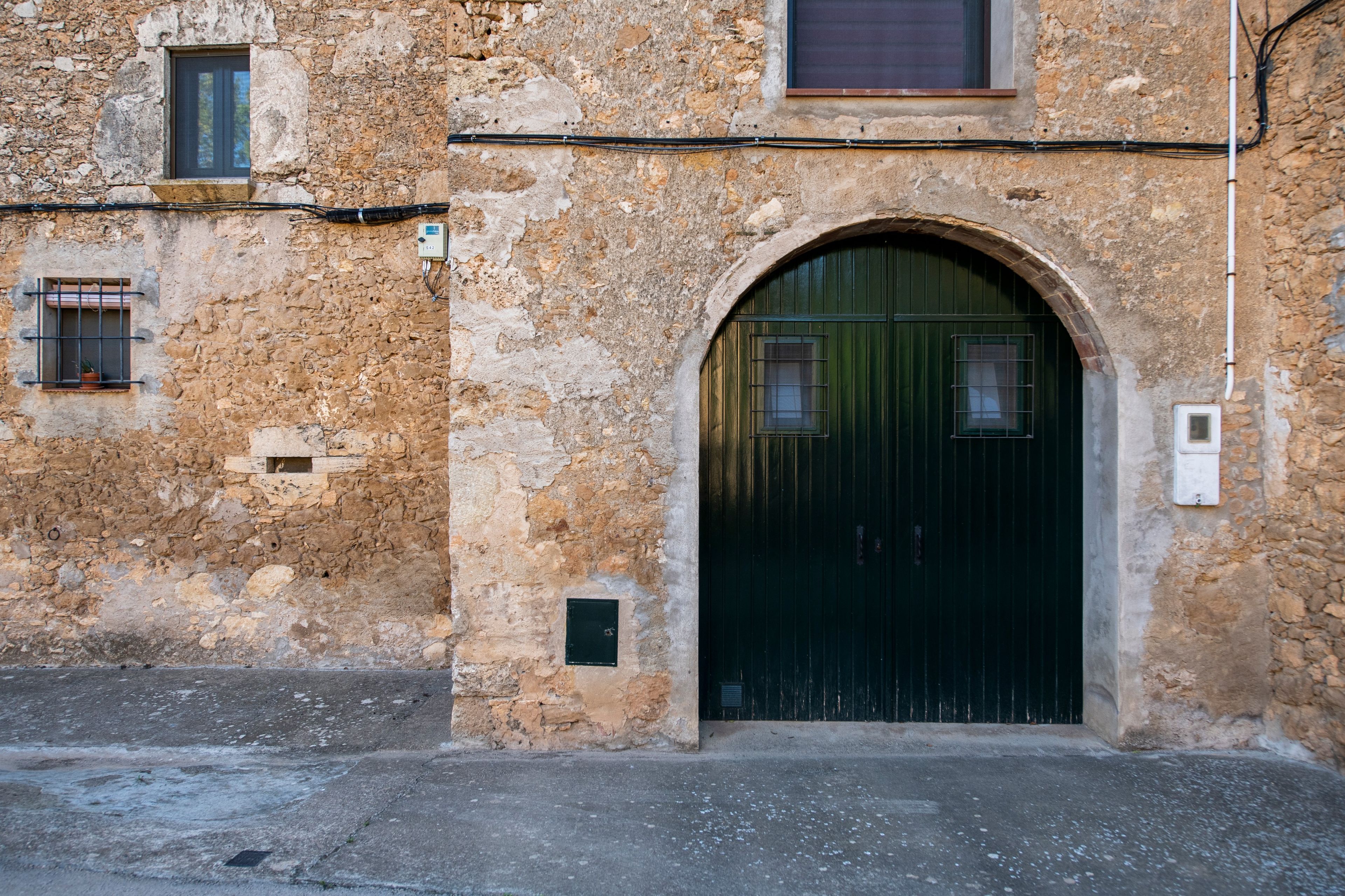 Un bâtiment doté d’une grande entrée en arc de cercle, d’une fenêtre ornée d’une grille métallique et d’un petit boîtier électrique fixé au mur.