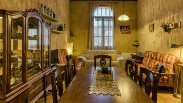Un comedor con una mesa de madera, sillas, un aparador con puertas de cristal, un sofá y una ventana con cortinas.