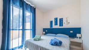 A bedroom with a bed, blue curtains, a nightstand, and wall art.