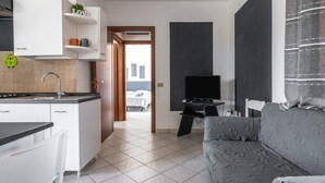 A compact living space with a kitchenette, a sofa, a TV, and a view of the city.