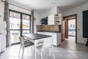 Una cocina moderna con armarios blancos, una zona de comedor con mesa y sillas, y vistas a través de un gran ventanal.