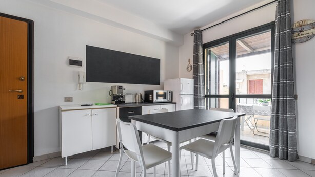A compact kitchen with a dining table and chairs, a refrigerator, a coffee maker, and a window with curtains.