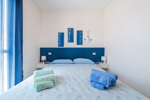Un dormitorio con cama, almohadas, mesita de noche, lámpara y un adorno en la pared.