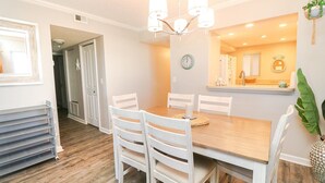 A dining area with a wooden table, white chairs, a chandelier, and a clock on the wall.