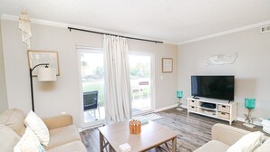A living room with a sofa, coffee table, TV, and a sliding glass door leading to an outdoor area.