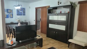 A modern living room with a flat-screen TV, a dark wooden cabinet, a dining area with chairs, and a small table with a vase. - Vacation Home 'La Quinta Adosado' with Sea View, Shared Pool & Wi-Fi (Santa Ursula)