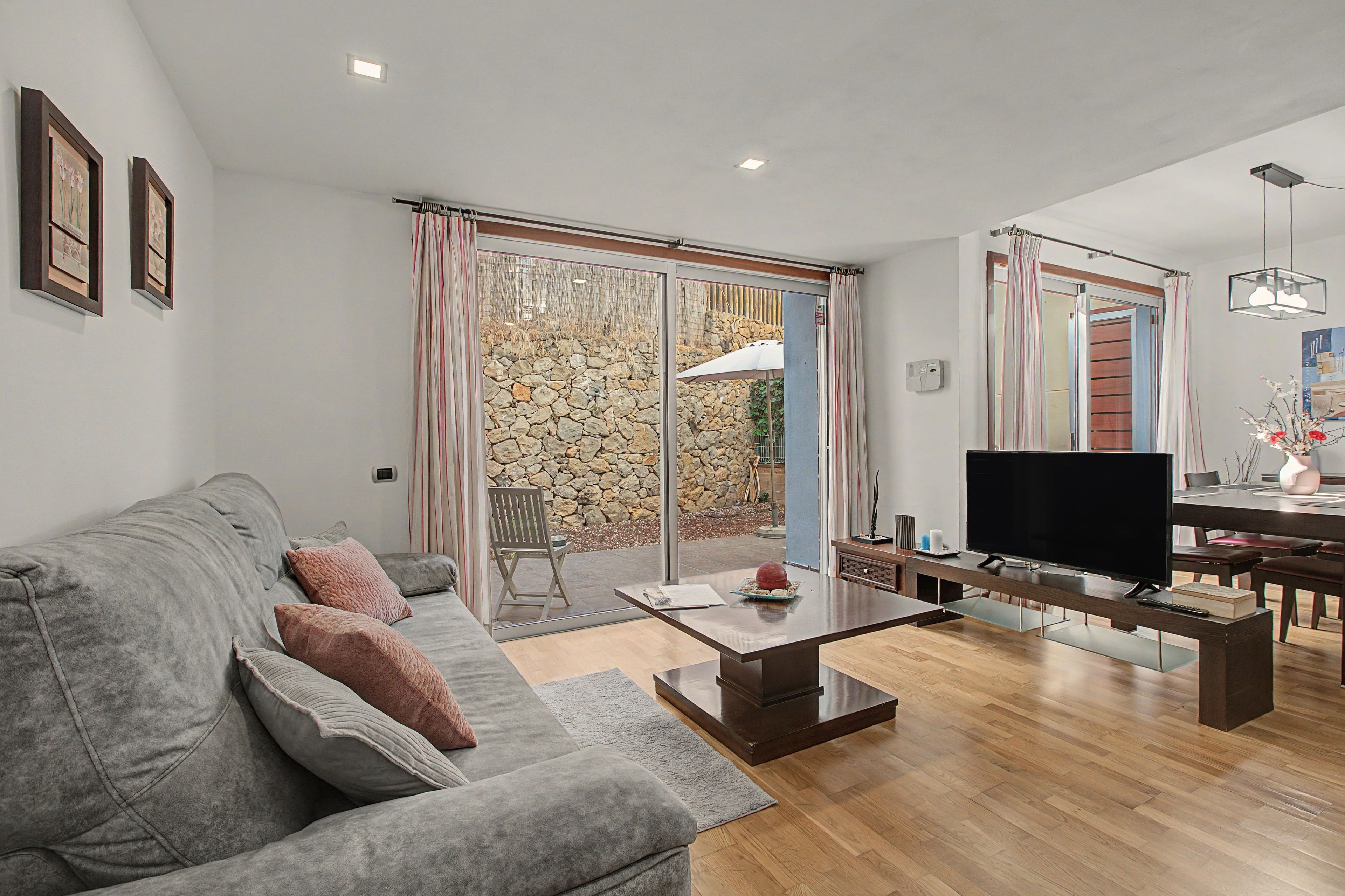 A modern living room with a grey sofa, a flat-screen TV, and a dining area with a table and chairs.