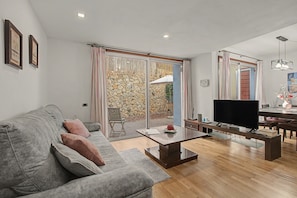 A modern living room with a grey sofa, a flat-screen TV, and a dining area with a table and chairs. - Vacation Home 'La Quinta Adosado' with Sea View, Shared Pool & Wi-Fi (Santa Ursula)
