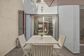 A patio with a table and chairs, a glass door leading to an interior space, and a stone wall. - Vacation Home 'La Quinta Adosado' with Sea View, Shared Pool & Wi-Fi (Santa Ursula)