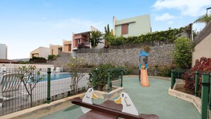A playground with a seesaw, a slide, and a pool. - Vacation Home 'La Quinta Adosado' with Sea View, Shared Pool & Wi-Fi (Santa Ursula)