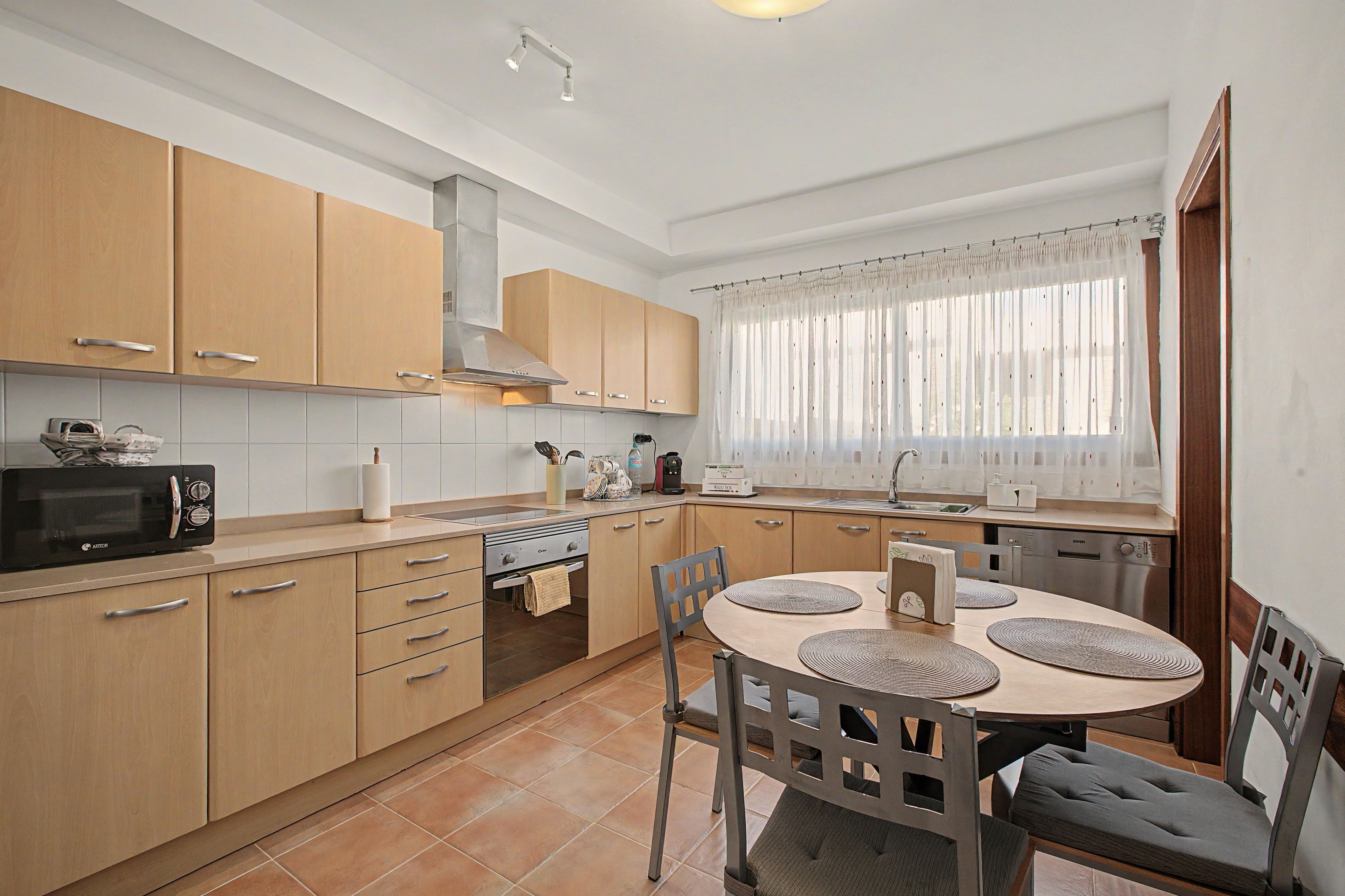 A modern kitchen with wooden cabinets, a built-in oven, a microwave, and a dining area with a round table and chairs.