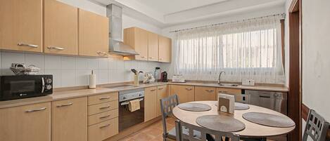 A modern kitchen with wooden cabinets, a built-in oven, a microwave, and a dining area with a round table and chairs.