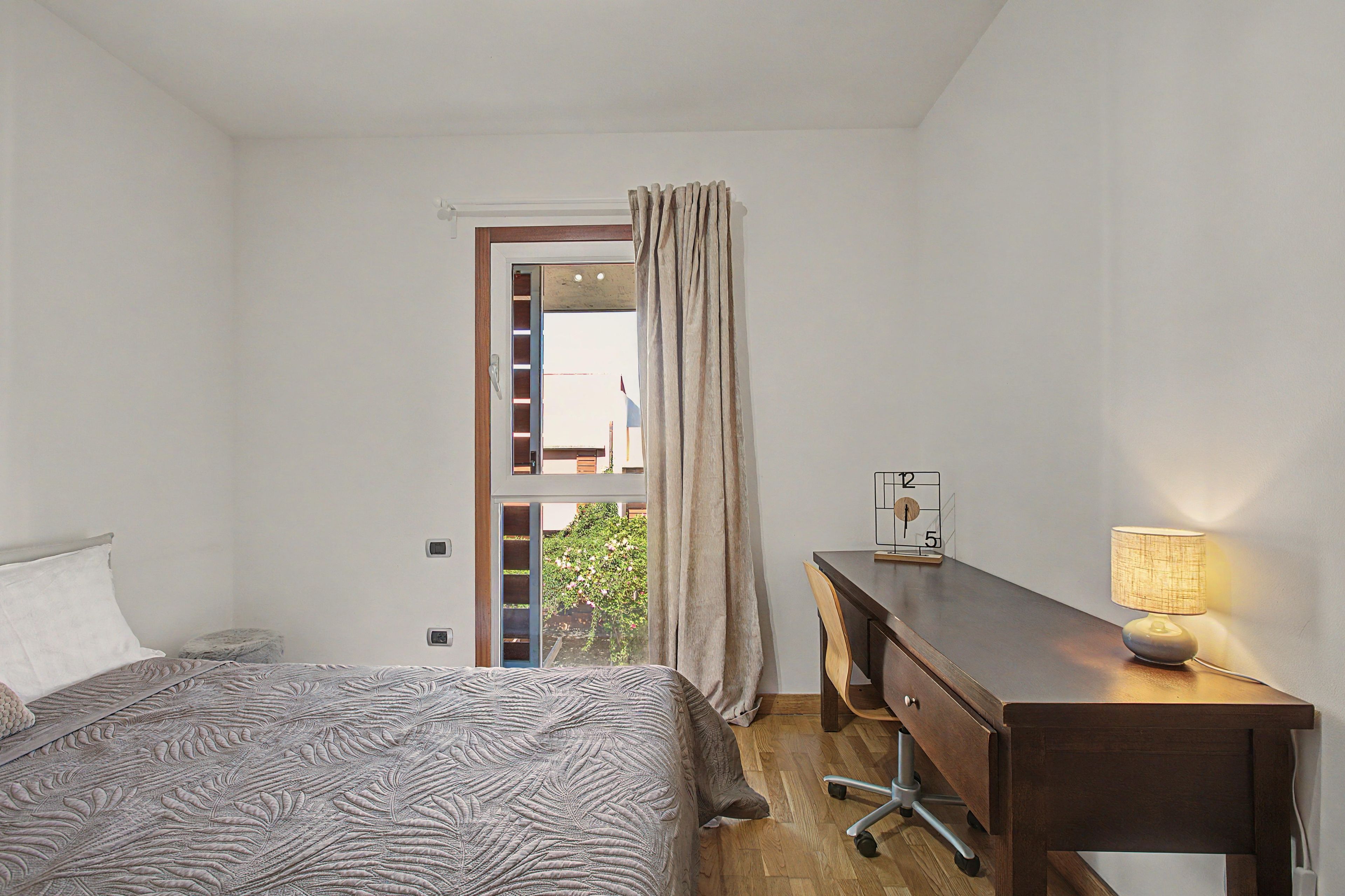 Een slaapkamer met een bed, een bureau, een stoel, een lamp en een uitzicht door een deur.